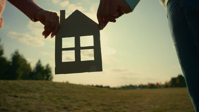 Happy family future Caucasian couple female male hands holding cardboard home outdoors sunshine village field. Spouses dreaming man woman buying new house real estate property mortgage housing renting