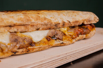 Panuozzo tradizionale campano ripieno di roast-beef, mozzarella e parmigiana di melanzane servito su un tagliere di legno in pub