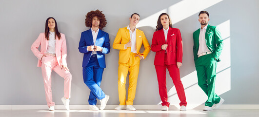 Portrait of a group of young business team in colorful suits standing against a grey wall. The image captures smiling faces, reflecting diverse and happy teamwork in a business setting.