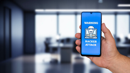 A Hacker Attack message on the mobile phone screen. Office image in the background. Close-up.