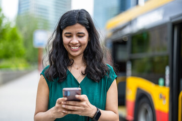 Young woman using smart phone at the bus stop in the city
