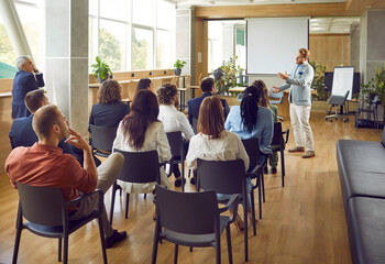 Confident business man speaking on a work meeting in the office in front of a diverse group of multiracial company employees or a team of staff sitting on chairs and listening to their leader.