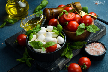 Italian Mozzarella cheese balls, basil and tomato cherry ready for cooking Caprese salad. On a dark stone background.