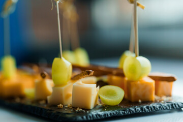 Slicing different types of cheese and grapes. Appetizer with cheese and grapes on a black board