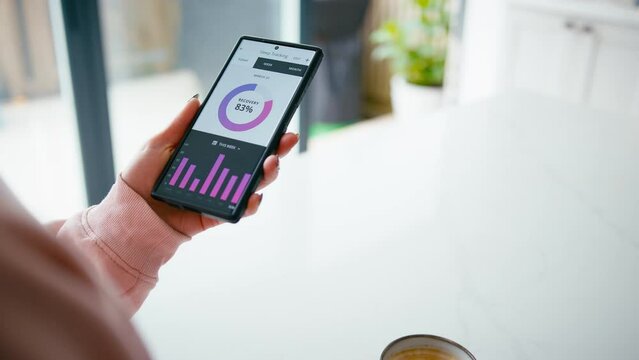 Close up of woman drinking coffee looking at sleep tracking app on mobile phone at home - shot in slow motion