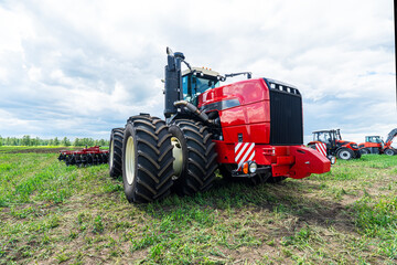 Obraz premium Close up of agriculture red tractor cultivating field over blue sky