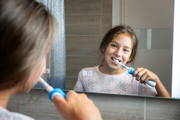 Happy little girl brushing her teeth in front of bathroom mirror. Morning hygiene.