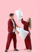 Young couple in pajamas fighting pillows on pink background