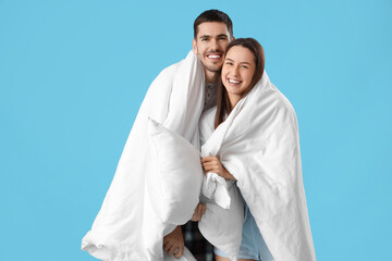 Young couple with blanket and pillows on blue background