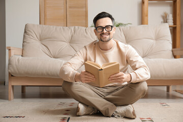 Young man in eyeglasses reading book in lotus position at home