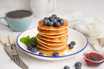 Plate with tasty pancakes, cup of tea and cutlery on white table