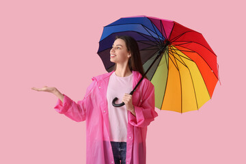 Young happy woman in raincoat with opened colorful umbrella on pink background