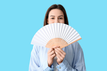 Young pretty woman with white hand fan on blue background