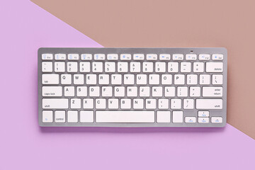 Grey computer keyboard on brown lilac background. Top view