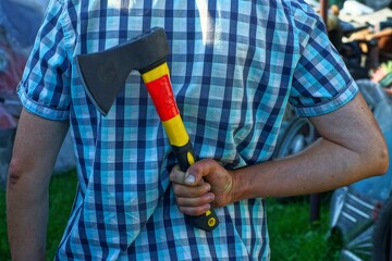 one sharp dangerous iron black small industrial hatchet with a yellow handle in the hand behind the...