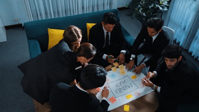 Top view of skilled businesswoman write marketing idea and placed sticky notes on mind mapping while planning financial strategy with diverse business group. Startup team working together. Directorate