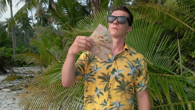Caucasian man holding Thai Baht on the beach in Thailand