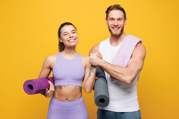 Young smiling happy strong fitness trainer instructor sporty two man woman wear blue clothes spend time in home gym hold yoga mat caremat isolated on plain yellow background Workout sport fit concept