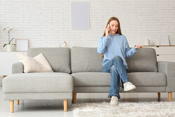 Obraz premium Young pretty woman talking with mobile phone on sofa in stylish living room