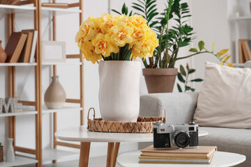 Vase with beautiful yellow narcissus flowers and photo camera on coffee table in living room