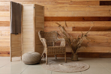Interior of stylish living room with rattan armchair, vase of pampas grass and folding screen near wooden wall