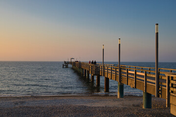 Obraz premium Hölzerne Seebrücke von Heiligendamm im sanften Abendlicht bei Sonnenuntergang, Blick über die ruhige Ostsee mit Spaziergängern, Mecklenburg-Vorpommern, Deutschland