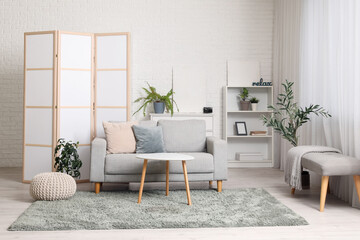 Interior of stylish living room with folding screen, grey sofa, shelving unit and coffee table