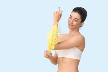 Beautiful young happy woman with soft feather on blue background. Depilation concept