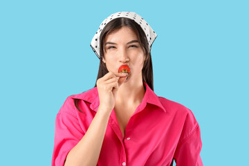 Beautiful young woman eating fresh strawberry on blue background