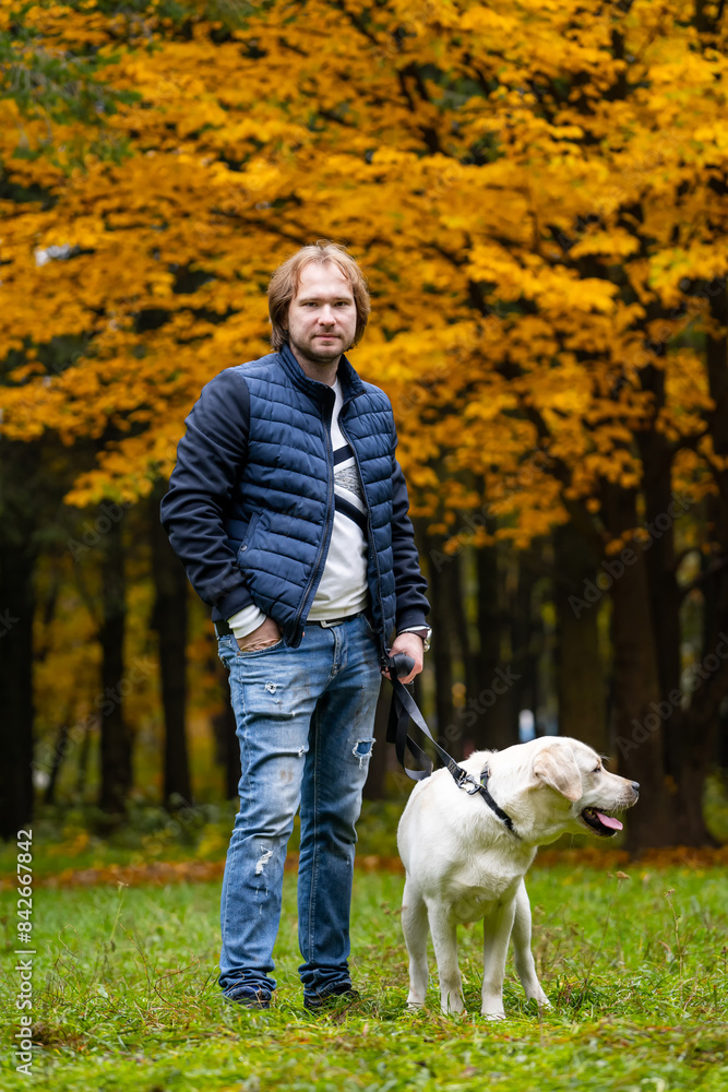 Poster a man is standing in a park with his dog. the man is wearing a black jacket and blue jeans. the dog 