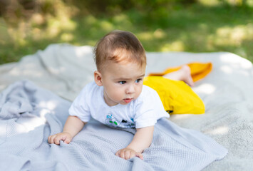 A baby is laying on a blanket in the grass. The baby is wearing a yellow skirt and a white shirt