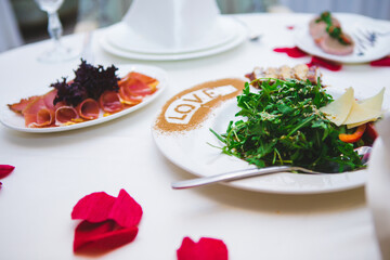 A plate of food with a love message written on it. The table is set with a variety of dishes, including a salad, meat, and bread.