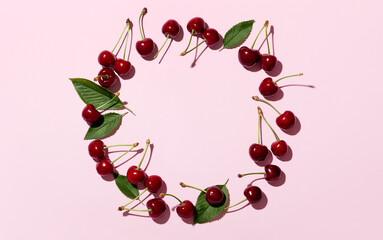 Round pink frame and ripe cherries on a pink background. Cherries or sweet cherries on a pink background. Top view. Space for text.