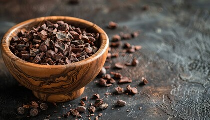 A wooden bowl filled with raw cocoa beans cacao nibs placed on a textured dark background