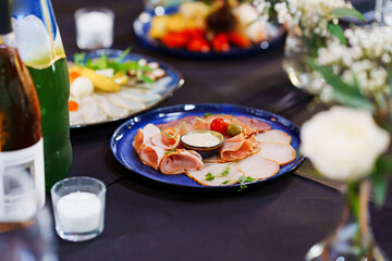 a plate of cold cuts and sauce on a served table with a black tablecloth. appetizers for the banquet.