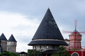 Gothic-style buildings with conical rooftops and a windmill in the background, set against a cloudy sky.