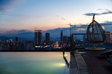 Sunset view of Da Nang, Vietnam, with high-rise buildings and a rooftop pool. A hanging chair adds...