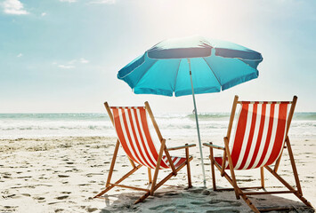 Rest, relax and beach chairs with umbrella on sand for vacation, holiday or weekend break. Summer, blue sky and seats in nature with water and ocean for peace, travel or tourism in bali getaway