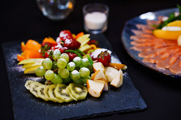 Plate with assorted fruit and powdered sugar on a banquet table with a black tablecloth.