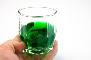 Hand holds a glass beaker with a green alcoholic drink on a white background. Glass beaker with a...
