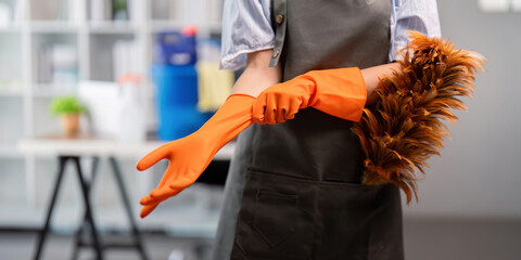 Female office cleaner putting on gloves with duster. Concept of workplace cleanliness