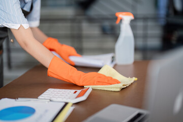 Female office cleaner wiping desk with cleaning supplies and documents. Concept of workspace maintenance
