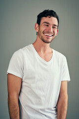 Obraz premium Smile, laughing and portrait of man in studio with funny joke, satisfaction and comedy meme. Relax, male person and face with happiness for humor, good mood and confidence on gray background