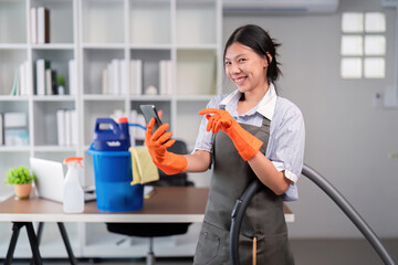 Smiling female office cleaner with vacuum and phone. Concept of workplace multitasking