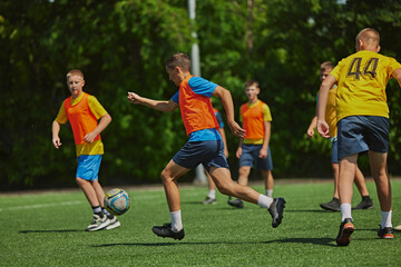 Obraz premium Teamwork in Action. Young soccer players in colorful uniforms playing soccer game outdoors on sunny day. Cooperation and competitive spirit. Sport, school, childhood, hobby, active lifestyle concept
