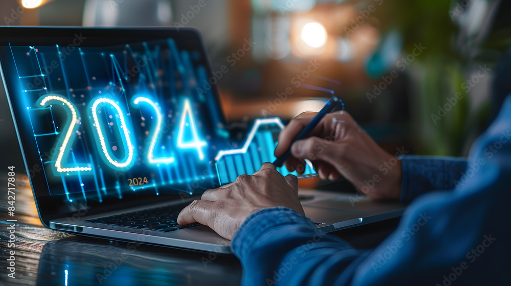Poster businessman using a laptop and drawing a growth graph with a hologram of the numbers 2024 on a virtu