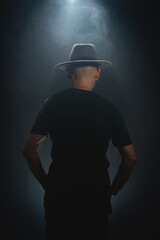 Mysterious, bearded man wearing a hat with his back to the camera. Studio portrait.
