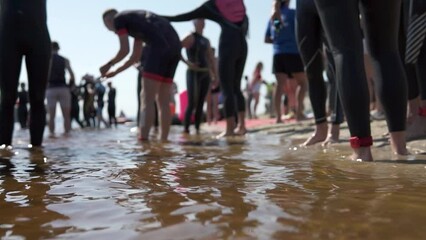 Triathletes stand on the beach, preparing for a marathon swim. Professional training for swimmers, open water triathlon competitions.
