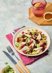 Healthy salad with boiled beets, chicken breast, iceberg lettuce, walnuts and peanut dressing on a ceramic plate on a gray concrete background. Salad recipes.