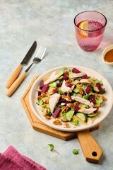 Healthy salad with boiled beets, chicken breast, iceberg lettuce, walnuts and peanut dressing on a ceramic plate on a gray concrete background. Salad recipes.